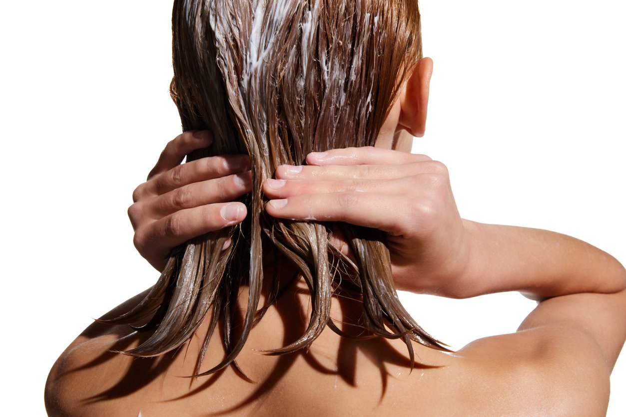 Blonde Frau von hinten, die ihre schulterlangen Haare mit einer Haarkur pflegt